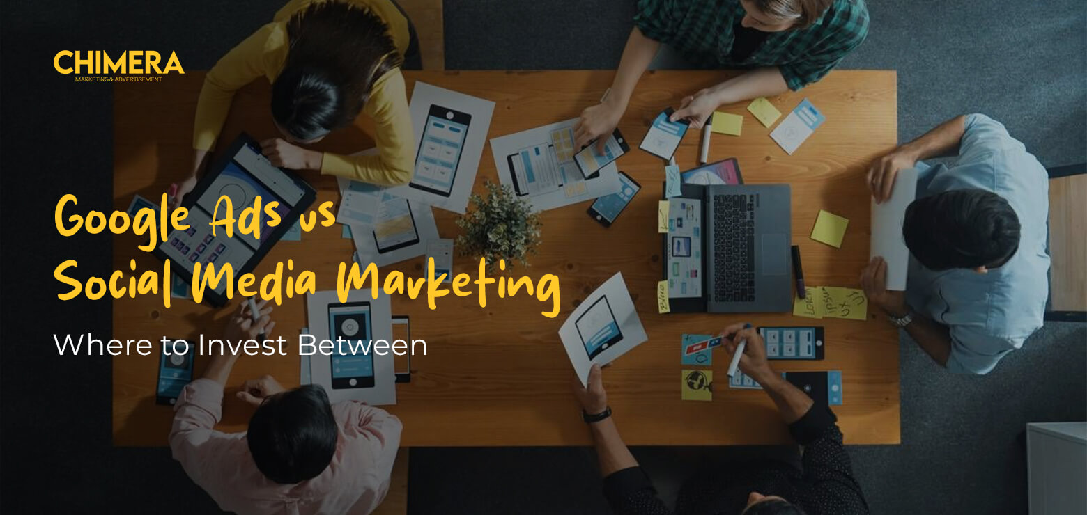 An overhead view of a creative team collaborating at a wooden table covered in UI/UX wireframes and digital sketches, featuring the Chimera Marketing logo and text overlay "Google Ads vs Social Media Marketing: Where to Invest Between.