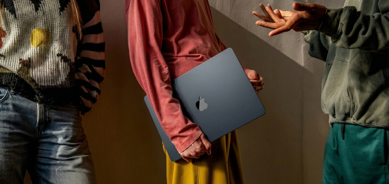 Three creative team members standing closely together during a strategic discussion, with one person holding a closed dark blue laptop while another gestures with open hands, illustrating an agency retainer audit framework