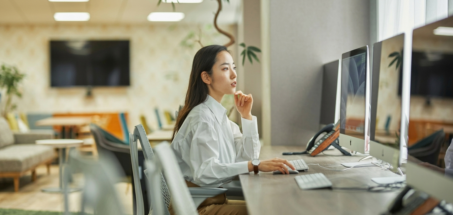 An Asian female SEO strategist in a crisp white shirt contemplating data on desktop monitors in a modern office, planning Generative Engine Optimization (GEO) strategies to replace keyword density with semantic entity density