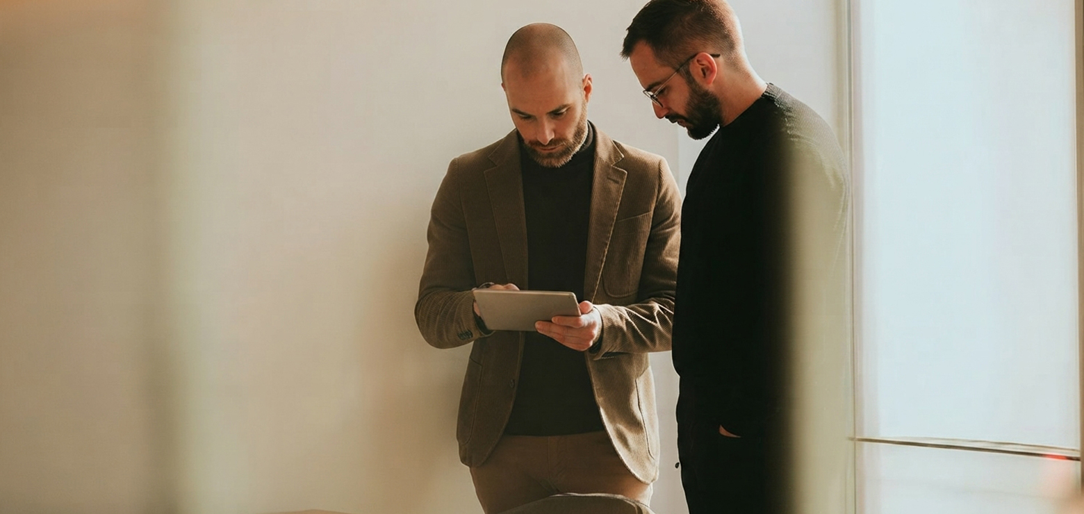 Two male marketing executives—one in a tan corduroy blazer interacting with a digital tablet and one in a black sweater and glasses—reviewing Generative Engine Optimization data for an AI SEO agency in Anaheim, CA
