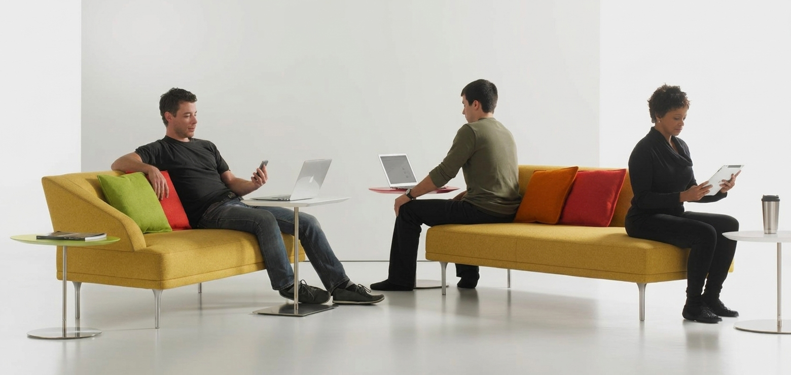 Three professionals sitting on modern yellow sofas in a bright, white studio, working on laptops, a smartphone, and a tablet with colorful accent pillows nearby, representing an enterprise teardown of AI SEO agencies and growth systems in Anaheim, Orange County