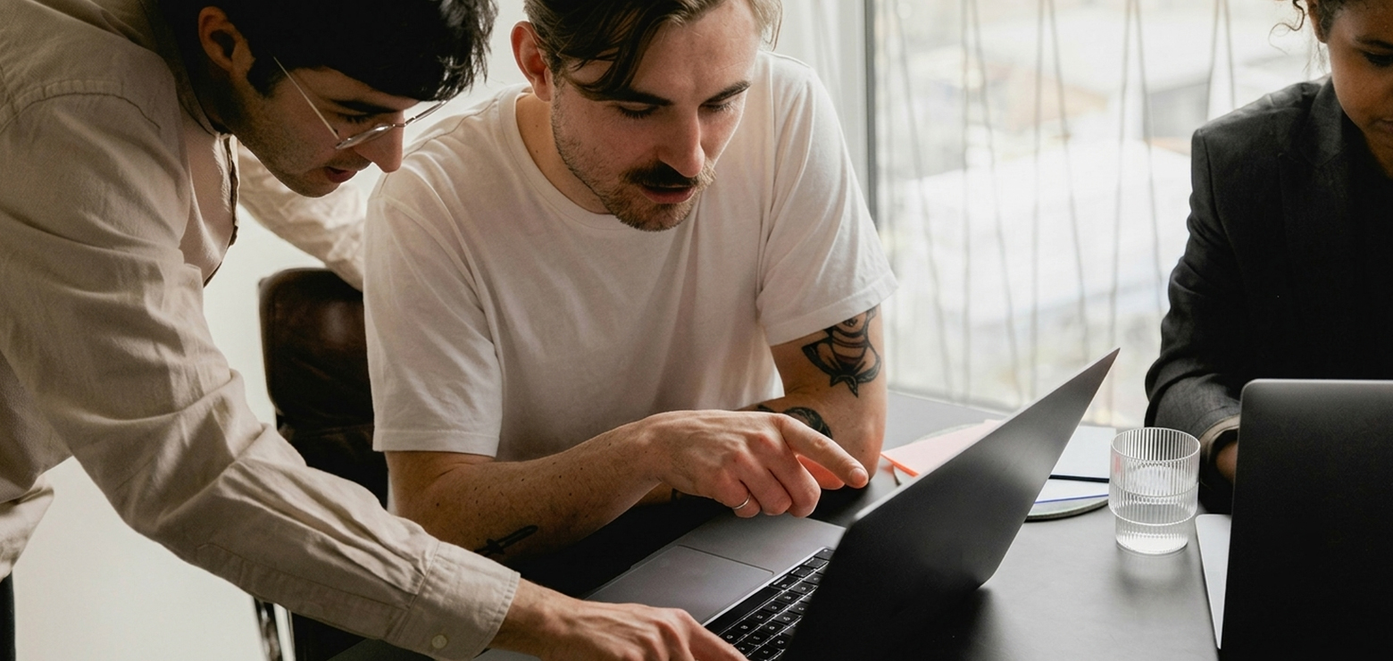 Two male digital strategists leaning over a dark office table focusing intently on a laptop screen while one points to data insights, illustrating zero-click search tactics and Google CTR recovery strategies for AI agencies in Anaheim, California