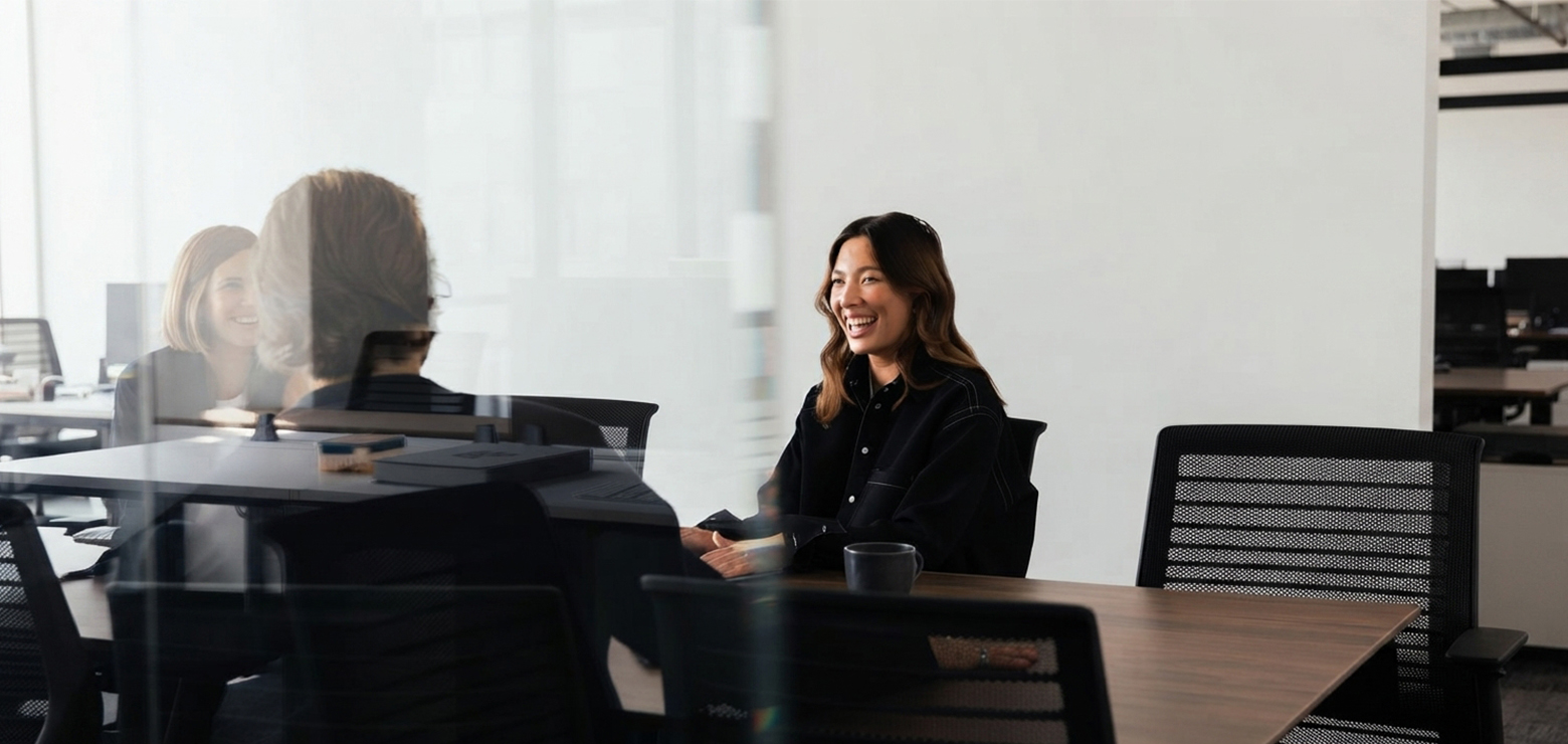 An Asian female marketing strategist in a dark shirt smiling during a strategy meeting in a glass-walled conference room, illustrating how an AI SEO agency in Anaheim, CA re-engineers brands for generative search engines