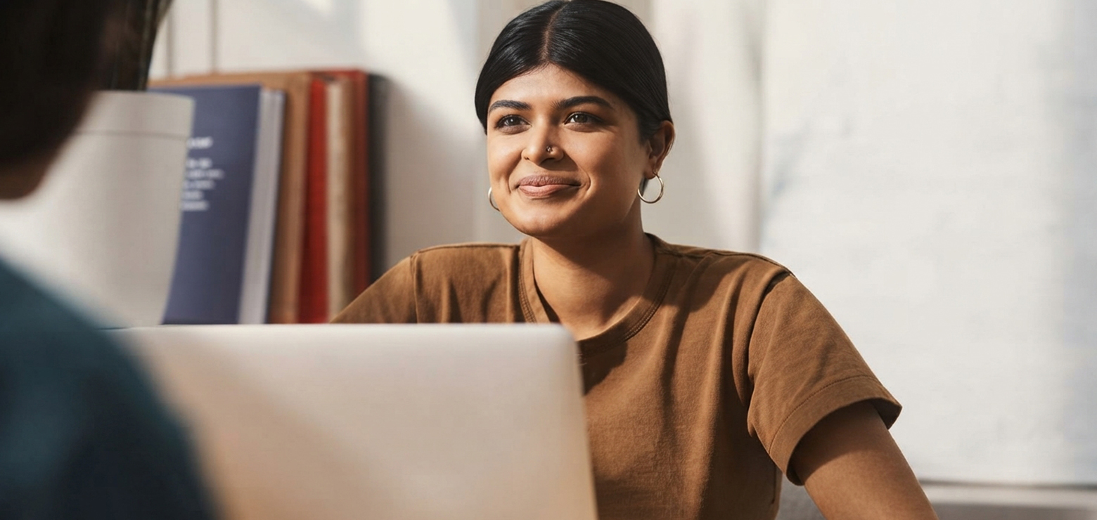 A South Asian female digital marketing strategist in a brown t-shirt smiling behind a laptop while advising a client during a consultation on optimizing for Retrieval-Augmented Generation and AI search citations