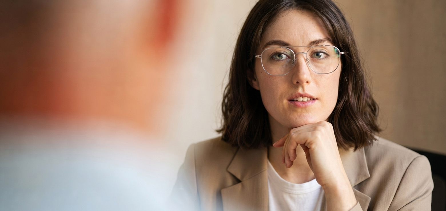 A female marketing strategist wearing wire-rimmed glasses and a beige blazer listening attentively during a client consultation, illustrating how Search Generative Experience impacts brand visibility in Anaheim, CA