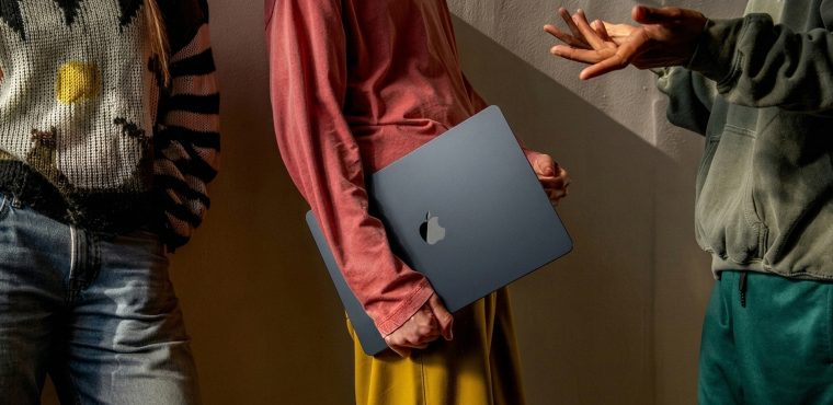 Three creative team members standing closely together during a strategic discussion, with one person holding a closed dark blue laptop while another gestures with open hands, illustrating an agency retainer audit framework