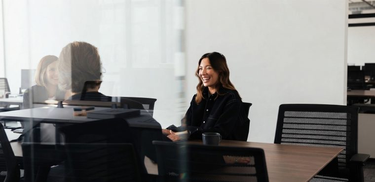 An Asian female marketing strategist in a dark shirt smiling during a strategy meeting in a glass-walled conference room, illustrating how an AI SEO agency in Anaheim, CA re-engineers brands for generative search engines