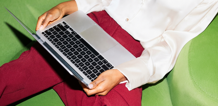 A top-down view of a digital growth strategist in a cream silk blouse and magenta trousers using a silver laptop while sitting on a bright green sofa, illustrating how Generative Engine Optimization captures high-paying enterprise clients in Irvine and Newport Beach