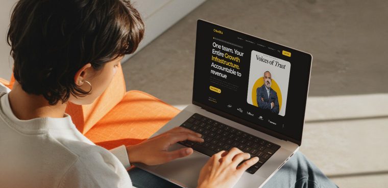 An over-the-shoulder view of a person typing on a laptop that displays The Chimera Marketing website homepage, featuring the headline "One team. Your Entire Growth Infrastructure. Accountable to revenue" alongside a "Voices of Trust" client testimonial card.