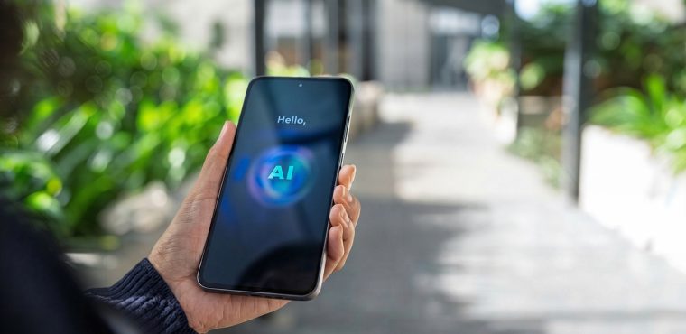 A person holding a smartphone outdoors displaying a glowing blue circular AI voice assistant interface with the text Hello, AI, evaluating Orange County agencies engineering web infrastructure for AI voice search in 2027