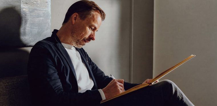 A male marketing strategist in a dark blazer taking notes in a journal during an executive planning session, illustrating the Orange County AI SEO playbook for generative engine recommendations in 2027