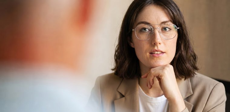 A female marketing strategist wearing wire-rimmed glasses and a beige blazer listening attentively during a client consultation, illustrating how Search Generative Experience impacts brand visibility in Anaheim, CA