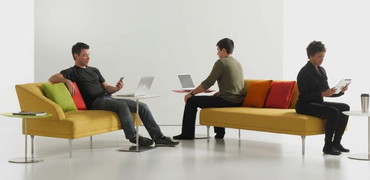 Three professionals sitting on modern yellow sofas in a bright, white studio, working on laptops, a smartphone, and a tablet with colorful accent pillows nearby, representing an enterprise teardown of AI SEO agencies and growth systems in Anaheim, Orange County