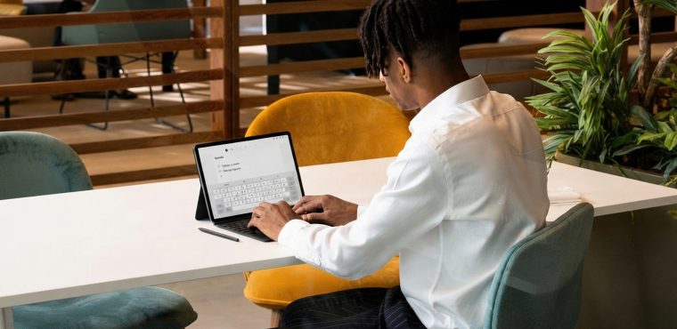 A young Black male digital strategist in a white dress shirt working on a 2-in-1 touchscreen tablet computer at a long white desk in a modern corporate workspace, analyzing why traditional SEO alone cannot capture AI search visibility